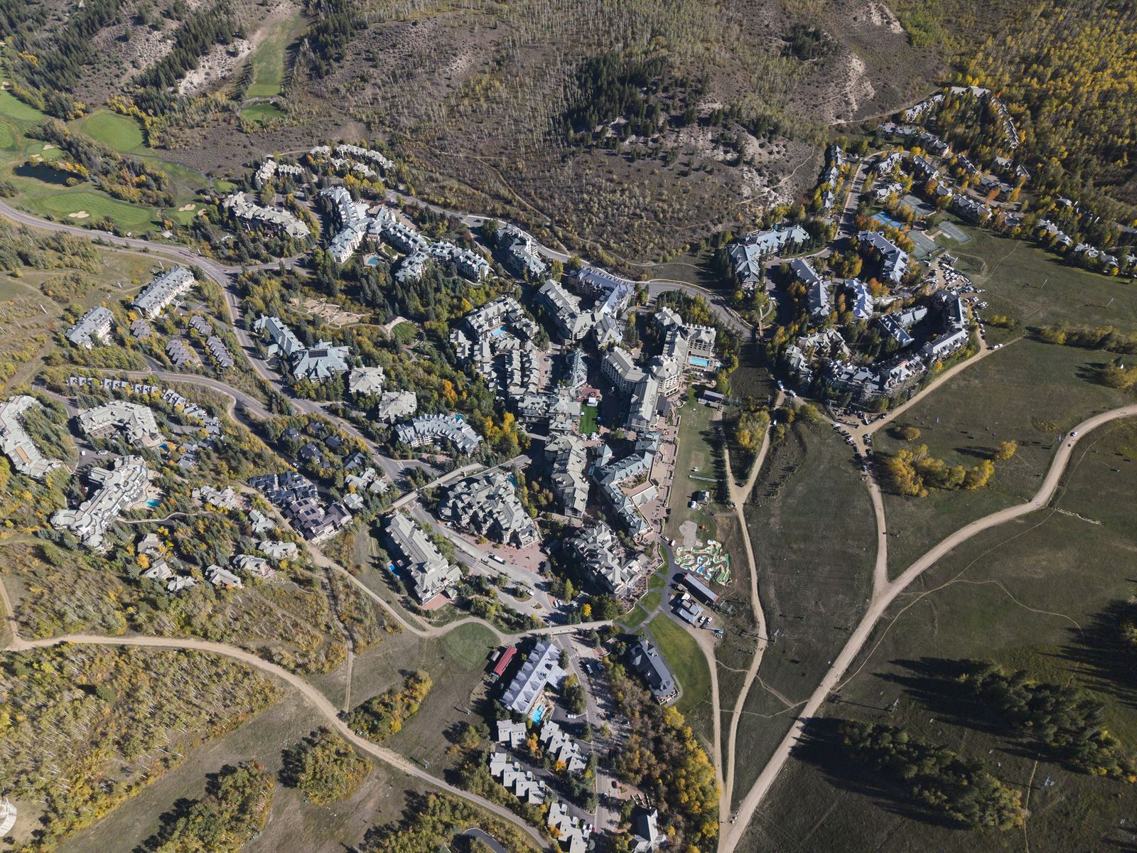 Aerial view of Beaver Creek village in early fall, lodges and condos clustered at the base of the ski slopes with golden aspen and dirt service roads across the mountainside