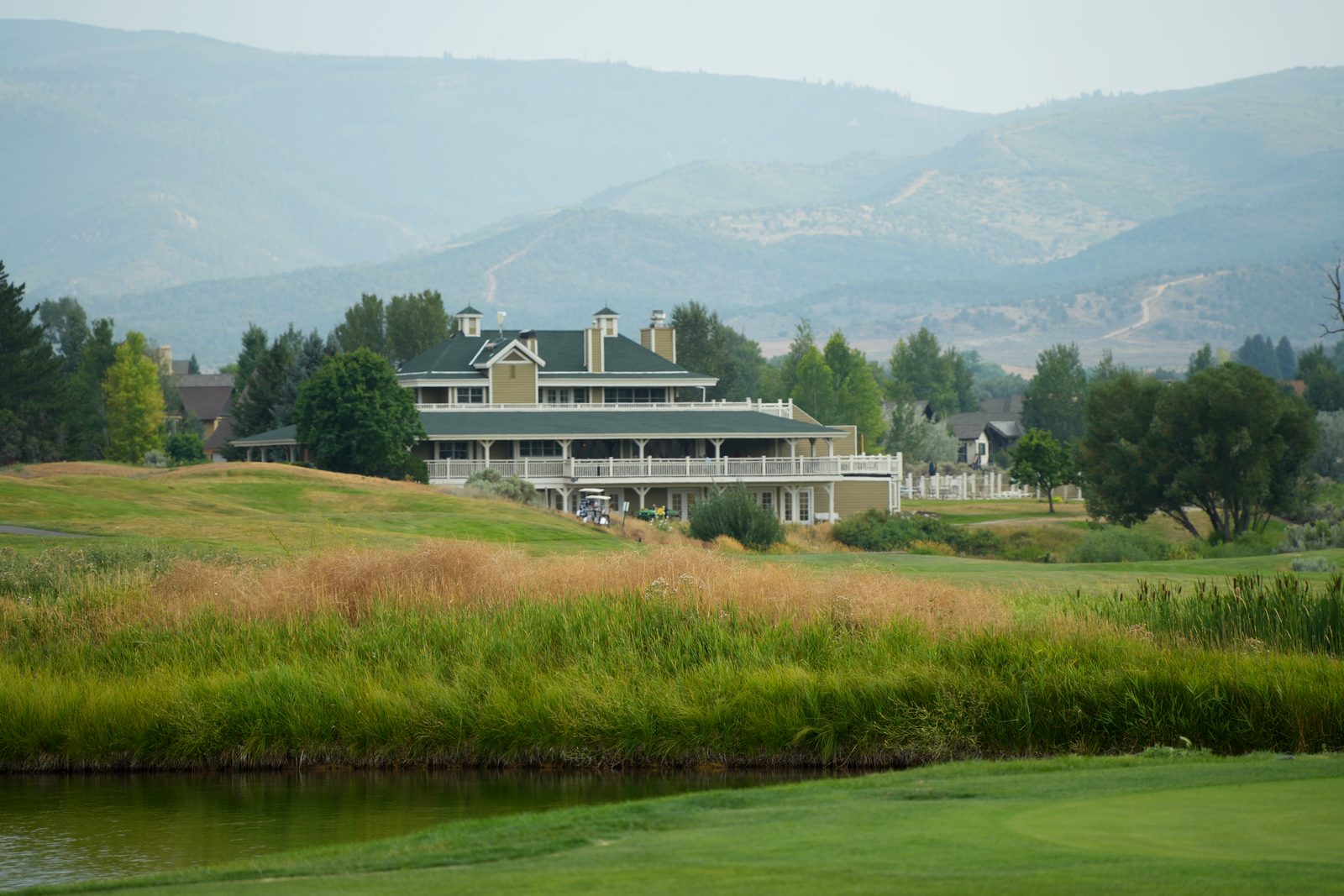 The clubhouse at Gypsum Creek Golf Course in Cotton Ranch, seen across a pond and rough grass, with the hills above the Eagle River Valley behind it