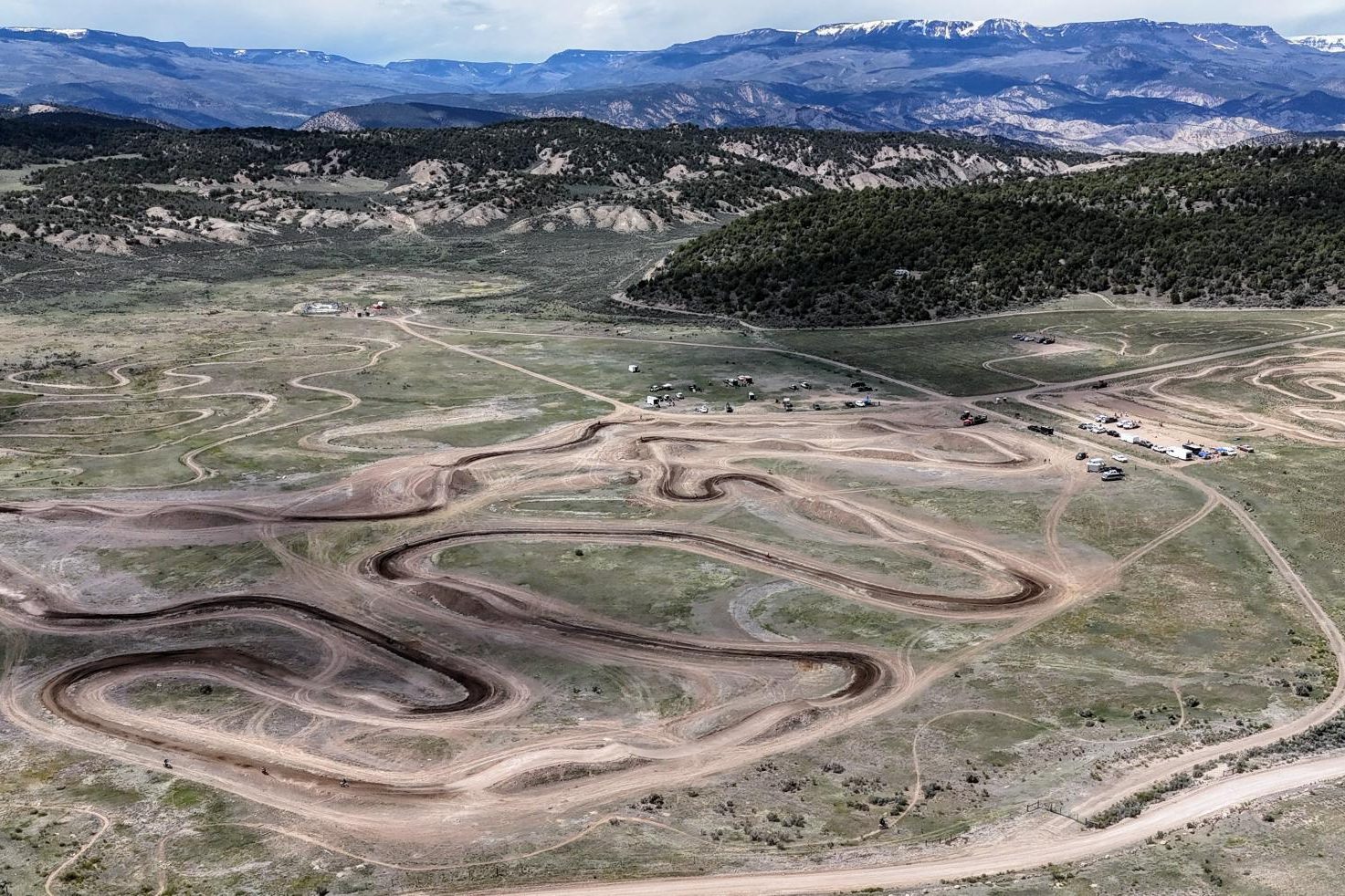 Aerial view of Dry Lake Motocross Park in Gypsum, Colorado, its winding dirt tracks spread across open sage country with forested hills and snow-capped peaks beyond