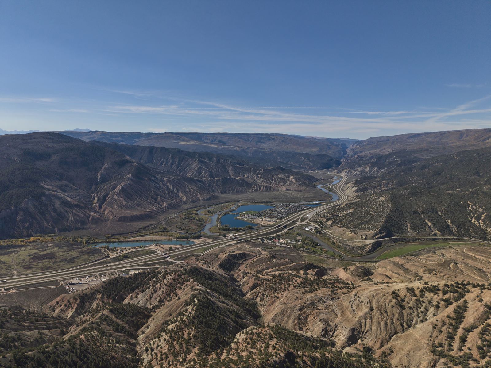 Aerial view west of Gypsum over juniper badlands, I-70, ponds and the river winding toward a distant canyon, with the Flat Tops on the horizon