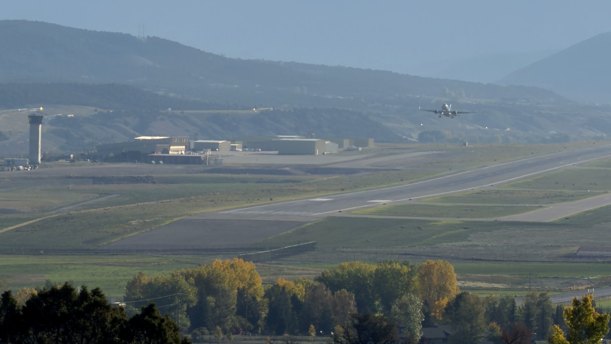 A jet lifts off the Eagle County Regional Airport runway in Gypsum, with the control tower and hangars on the left and fall cottonwoods in the foreground