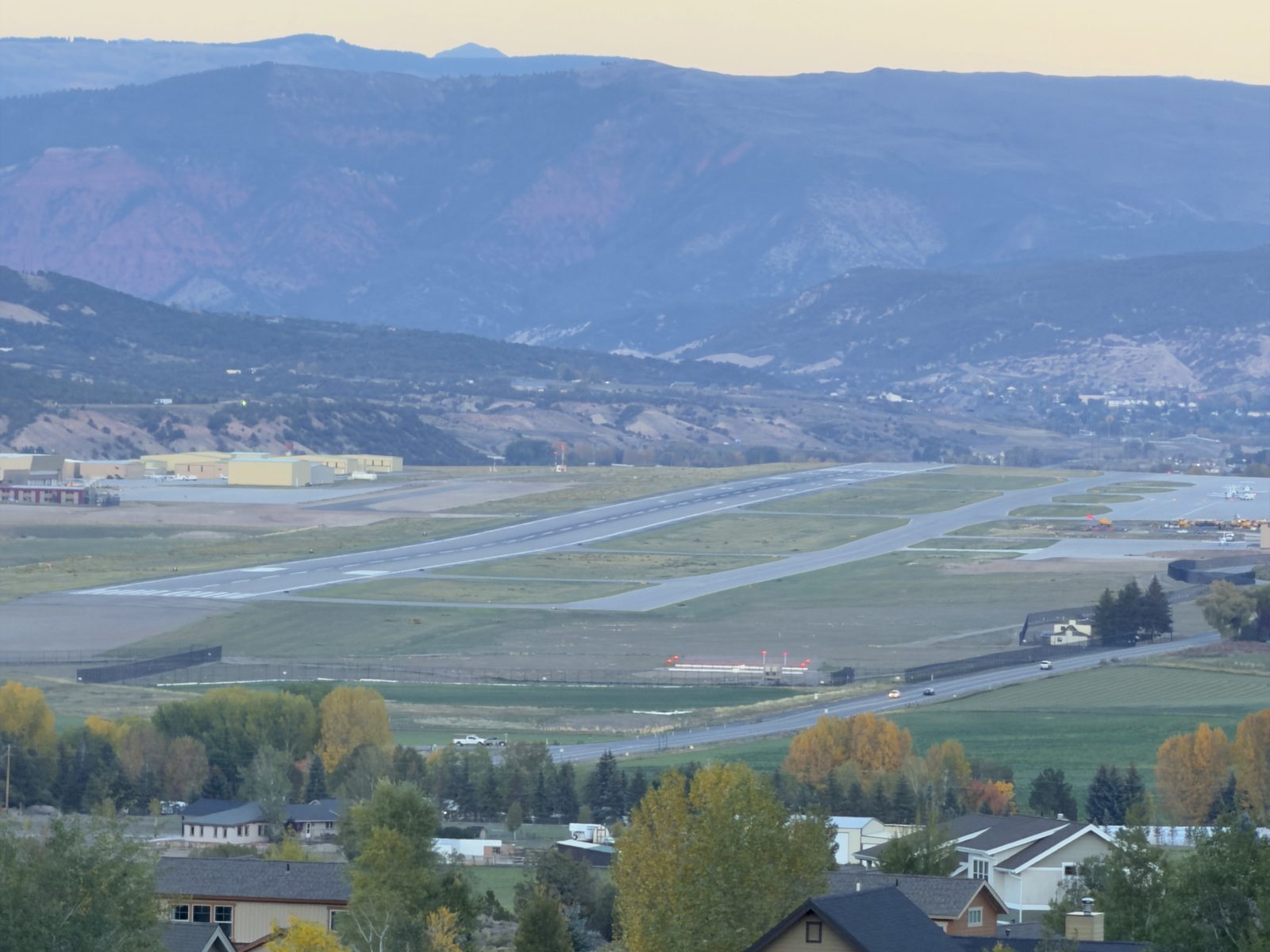 The Eagle County Regional Airport runway and hangars at dusk, with fall cottonwoods and homes in the foreground and red-rock mountains beyond