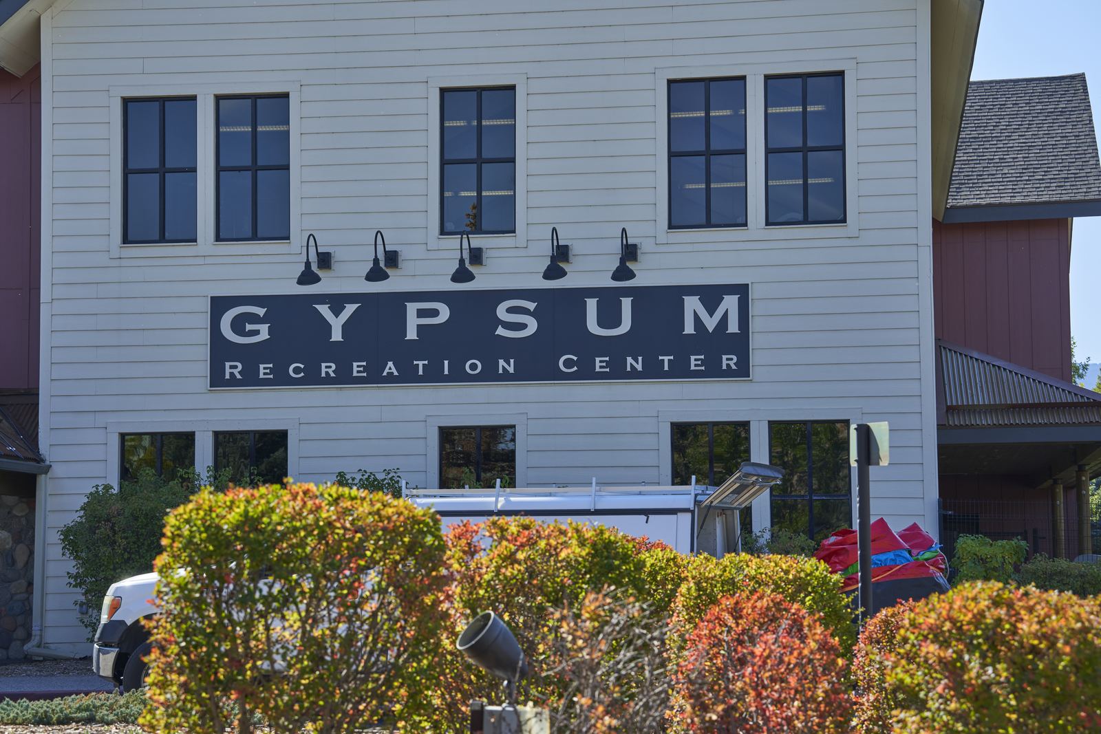 The front of the Gypsum Recreation Center, white siding and its name in large letters above fall-colored shrubs