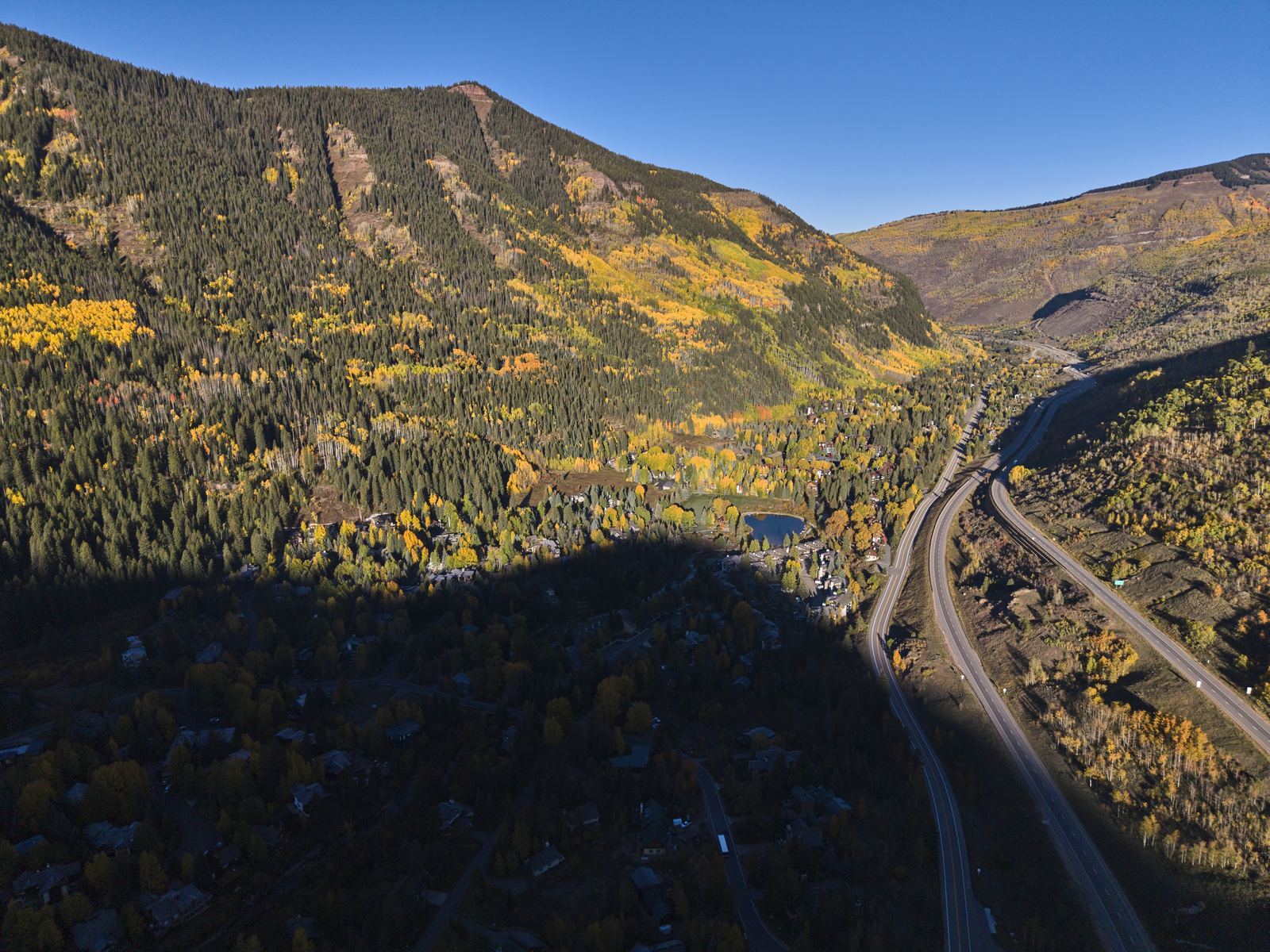 Aerial view of Interstate 70 curving through the Vail area in fall, with gold aspens across the mountainside above the highway