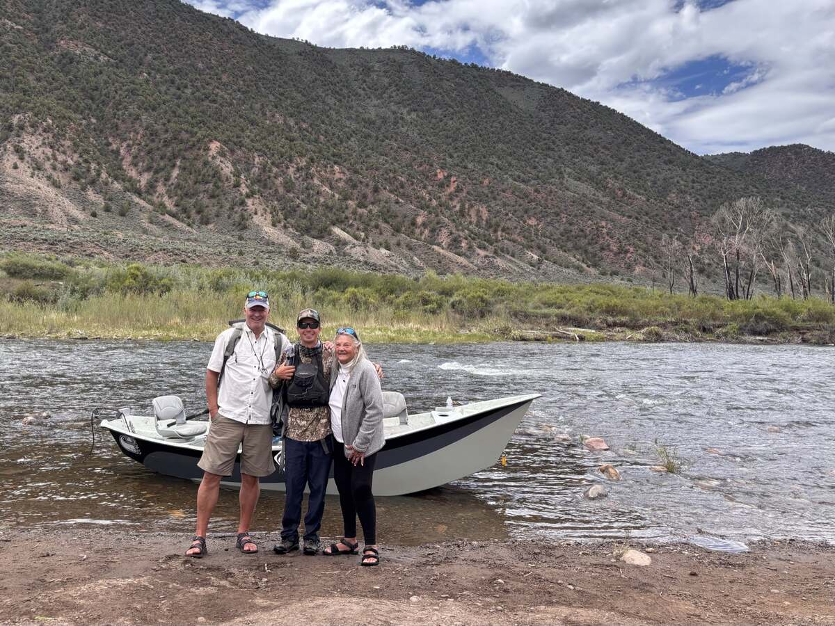 A guided drift boat pulled up on the gravel bank of the lower Eagle River downstream from Gypsum, with three anglers beside it and sage covered hills rising behind