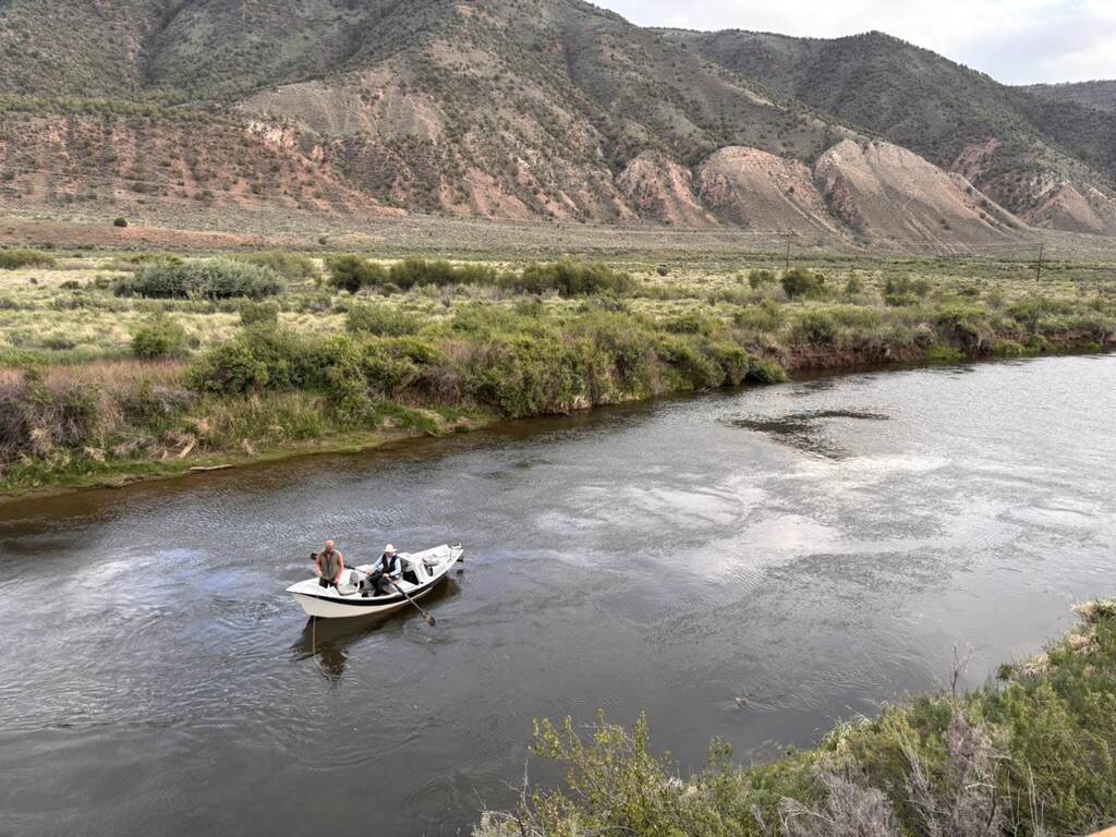 A drift boat floating the lower Eagle River downstream from Gypsum, Colorado, below eroded red and tan hills