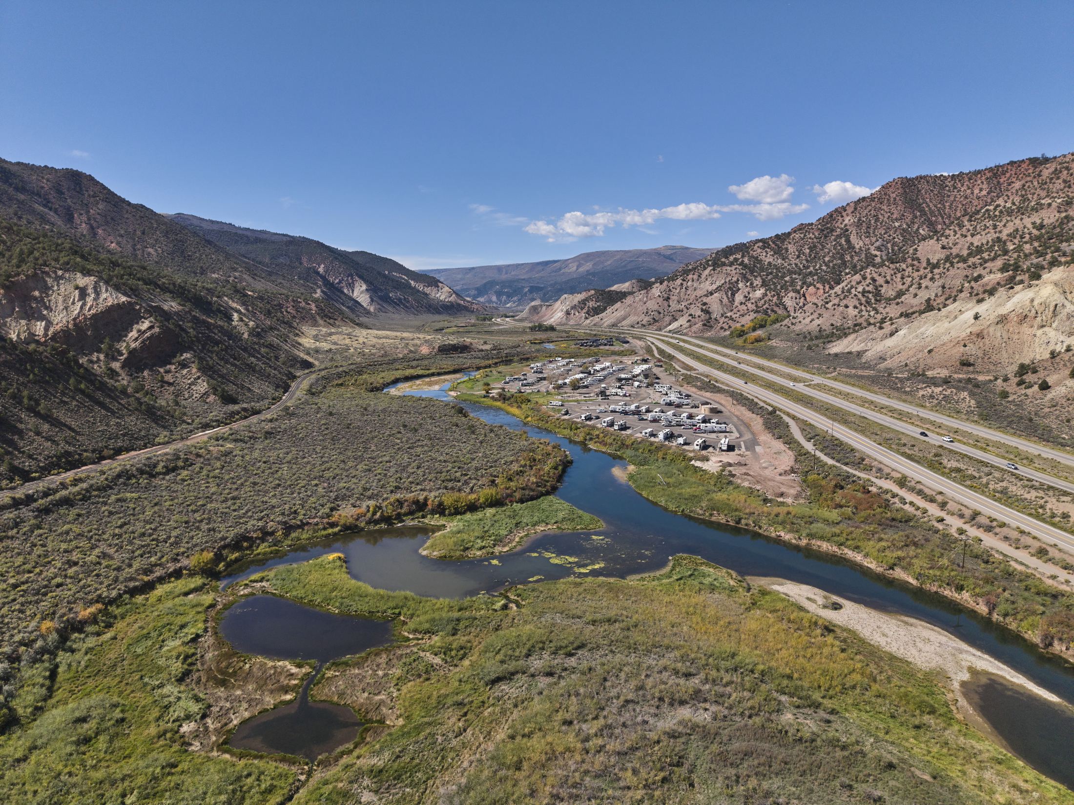Aerial view of the lower Eagle River winding through sage and wetland ponds below Gypsum in early fall, with I-70 and red and white hills alongside