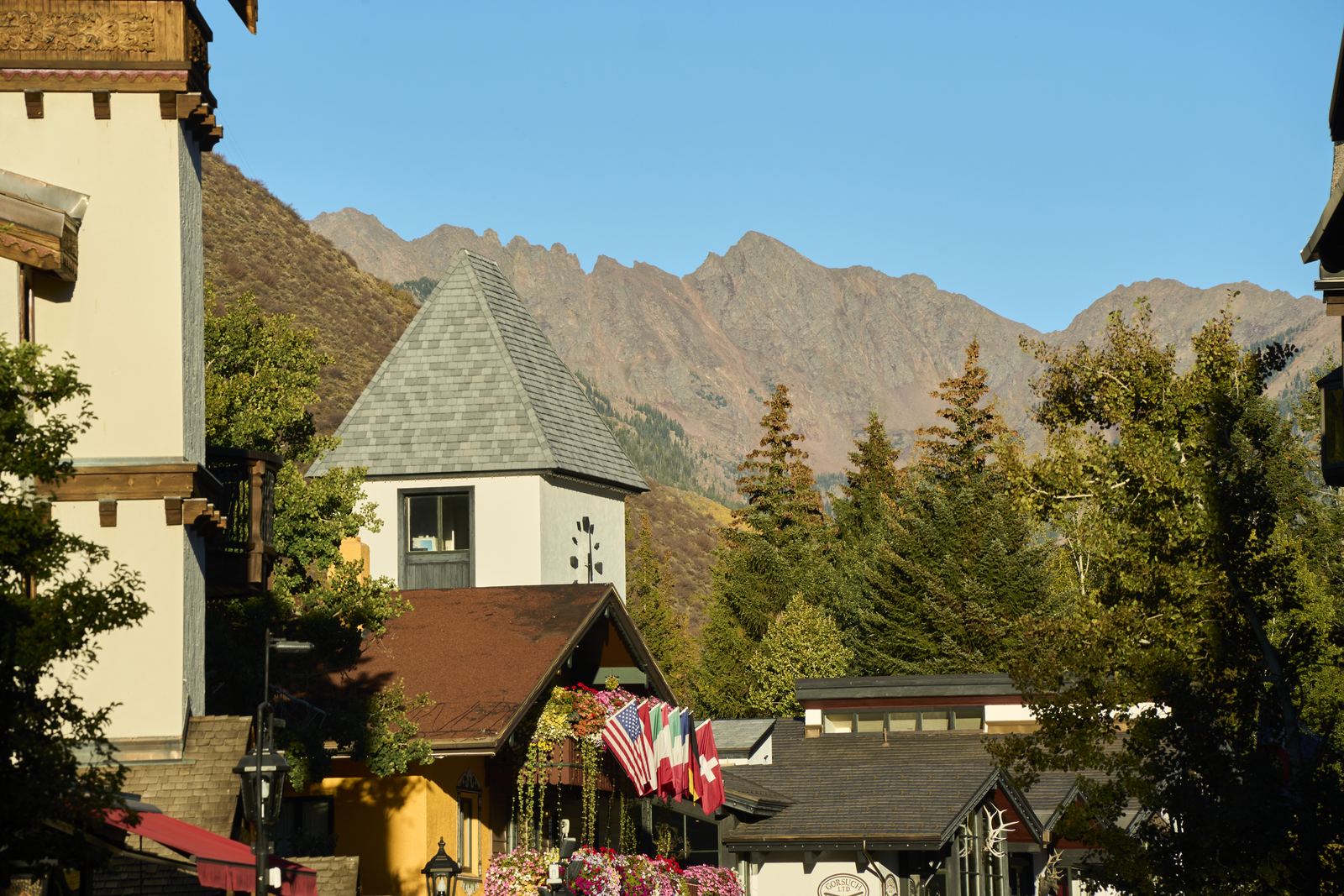 Vail Village in fall, a gabled tower and flower boxes with flags along the rooftops, with jagged peaks rising behind in late-afternoon light